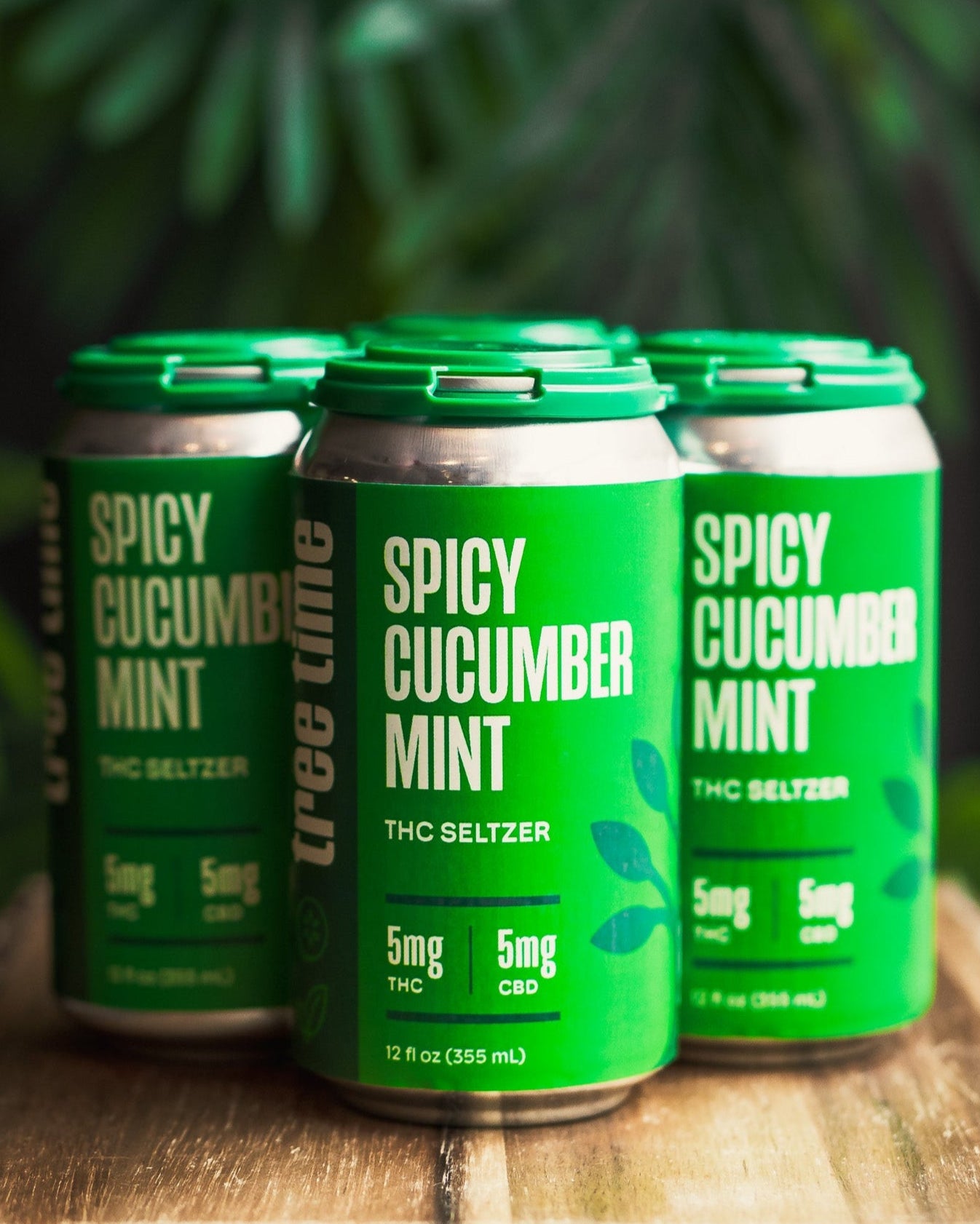 Four cans of Spicy Cucumber Mint THC Seltzer on a wooden surface with a green leafy background.