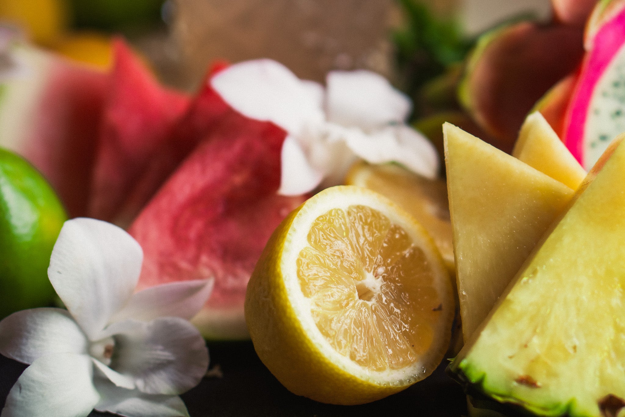 Close-up of sliced lemon, pineapple, dragon fruit, and watermelon with floral garnish – vibrant flavors in Tree Time sparkling THC drinks.